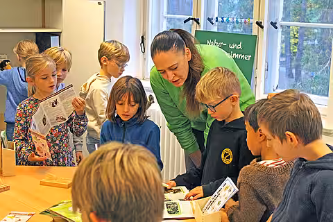 Eröffnung des Tierschutzzimmers in der Zinnowwald Grundschule in Berlin Zehlendorf Die aktion tier-Mitarbeiterin steht mit Kindern an einem Tisch und redet mit ihnen über Informationsmaterial.