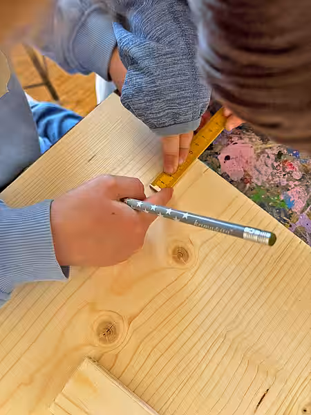 Mit viel Motivation wurden die Igelhäuser gebaut. Zwei Kinderhände am Igelhaus. Eines hält ein Lineal und einen Bleistift.
