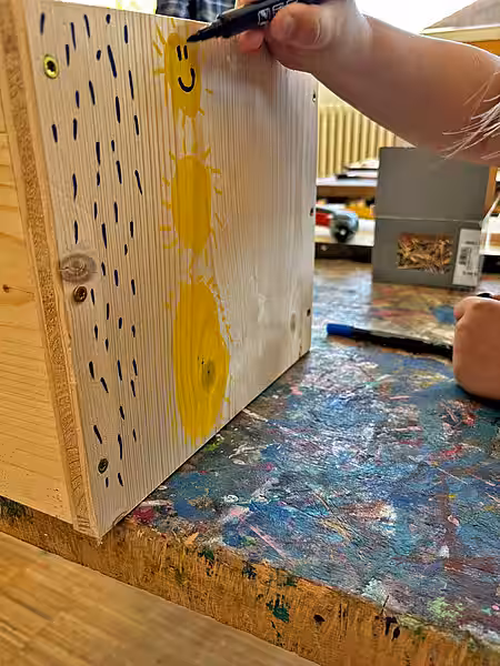 Dieses Haus wurde für die Auswilderung bestimmt. Kinderhände malen Sonnen auf das Holz des Igelhauses.