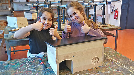 Der Tierschutzunttericht gehört zum Projekt JUNIOR von aktion tier. Zwei Kinder, die stolz ein selbstgebautes Igelhaus präsentieren.
