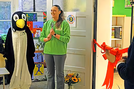 Eröffnung des Tierschutzzimmers in der Zinnowwald Grundschule in Berlin Zehlendorf Eine Frau in grünem Pullover und ein Pinguin-Maskottchen stehen vor der roten Schleife in der Tür.