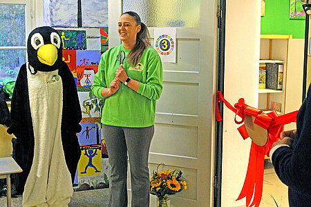 Eröffnung des Tierschutzzimmers in der Zinnowwald Grundschule in Berlin Zehlendorf Eine Frau in grünem Pullover und ein Pinguin-Maskottchen stehen vor der roten Schleife in der Tür.
