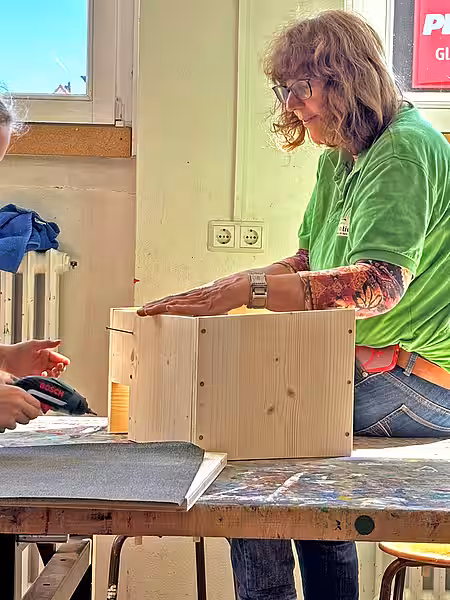 Unsere Tierschutzlehrerin erklärt die Funktion eines Igelhauses. Mitarbeiterin in grünem Shirt sitzt neben einem Igelhaus und redet.