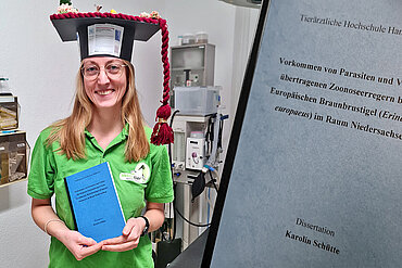 Eine lächelnde Frau mit Doktorhut und ihre Doktorarbeit.