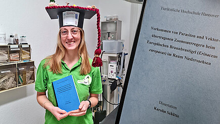 Eine lächelnde Frau mit Doktorhut und ihre Doktorarbeit.