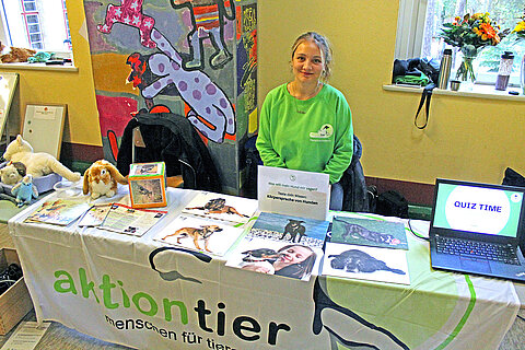 Eröffnung des Tierschutzzimmers in der Zinnowwald Grundschule in Berlin Zehlendorf Eine Frau im grünen Pullover sitzt an einem Tisch mit aktion tier-Banner und Informationsmaterialien darauf.