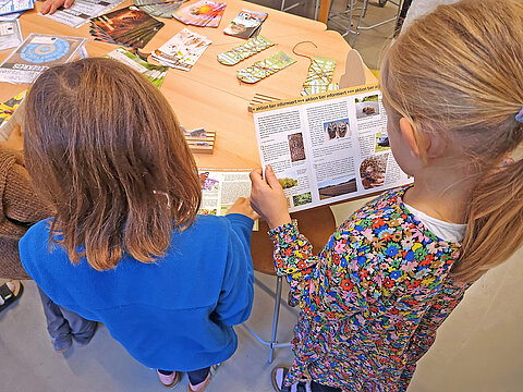 Eröffnung des Tierschutzzimmers in der Zinnowwald Grundschule in Berlin Zehlendorf Zwei Mädchen stehen an einem Tisch mit Informationsmaterial, eins liest in einer Broschüre.