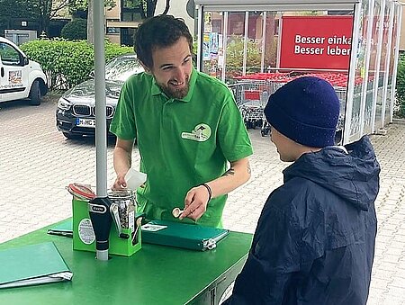 Sead vom Team Bayern füllt einer Passantin eine Portion INSEKTENSCHMAUS ab.